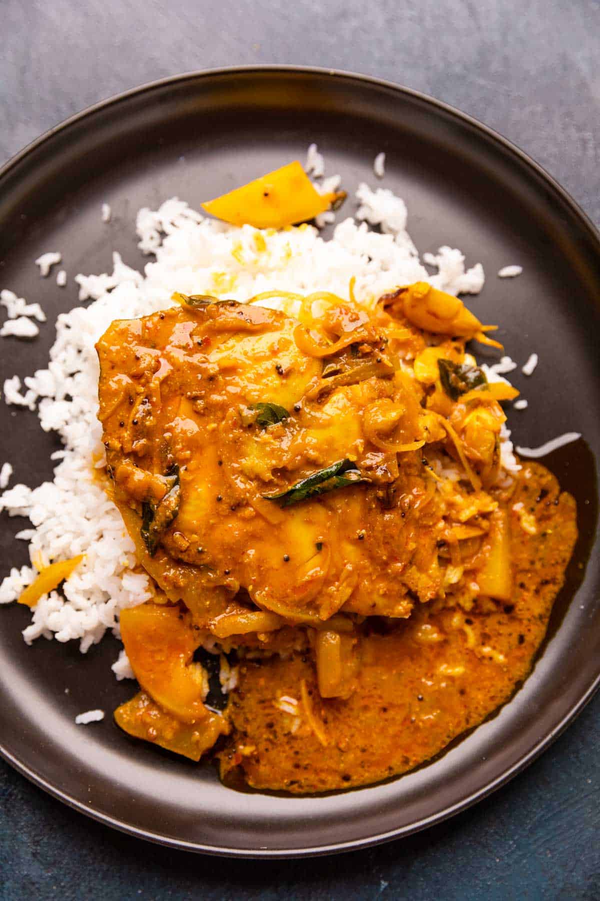 A plate of rice with raw mango fish curry on top of the rice