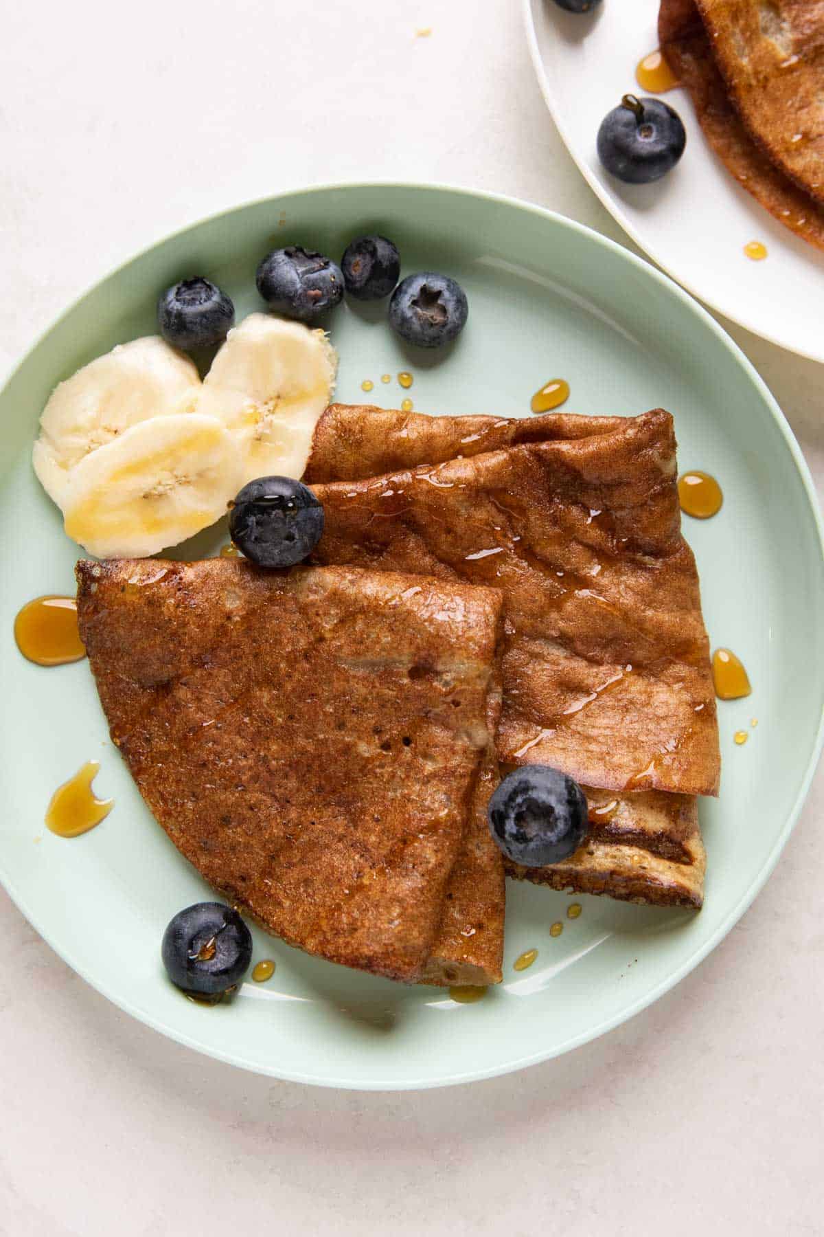 Banana Dosa served on a green kids plate with bananas, honey and blueberries on the side