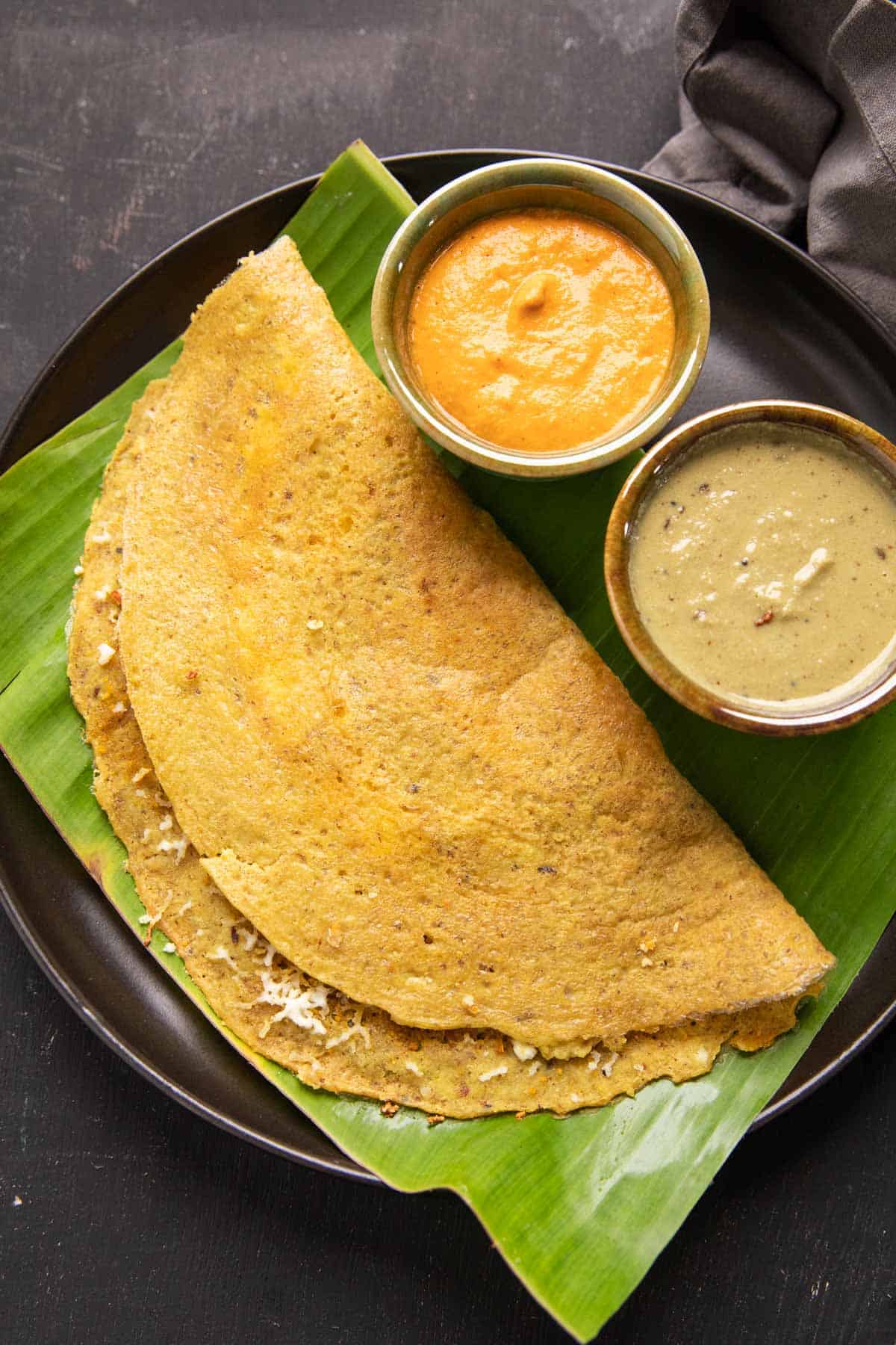 High Protein Dosa served on a banana leaf with chutney and curry on the side