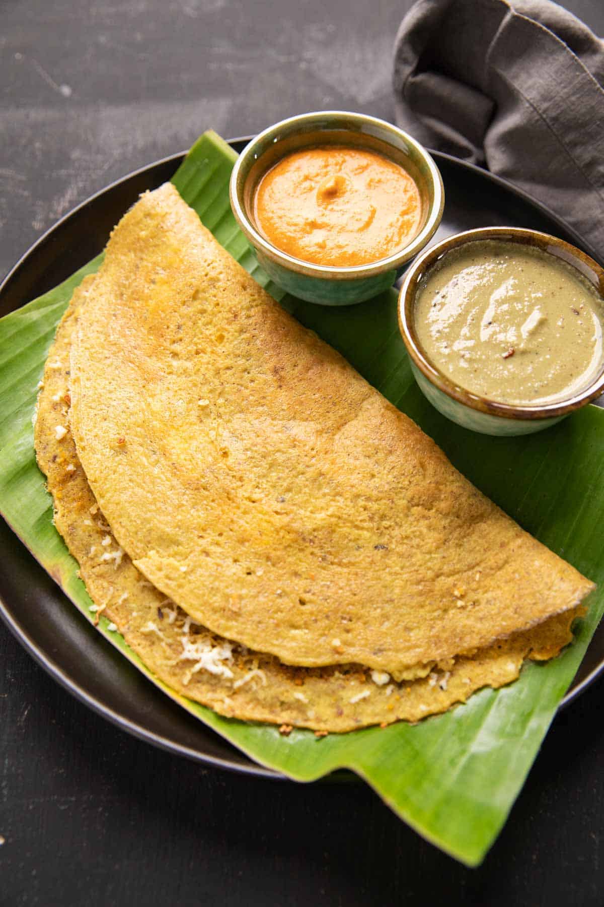 High Protein Dosa served on a banana leaf with chutney and curry on the side