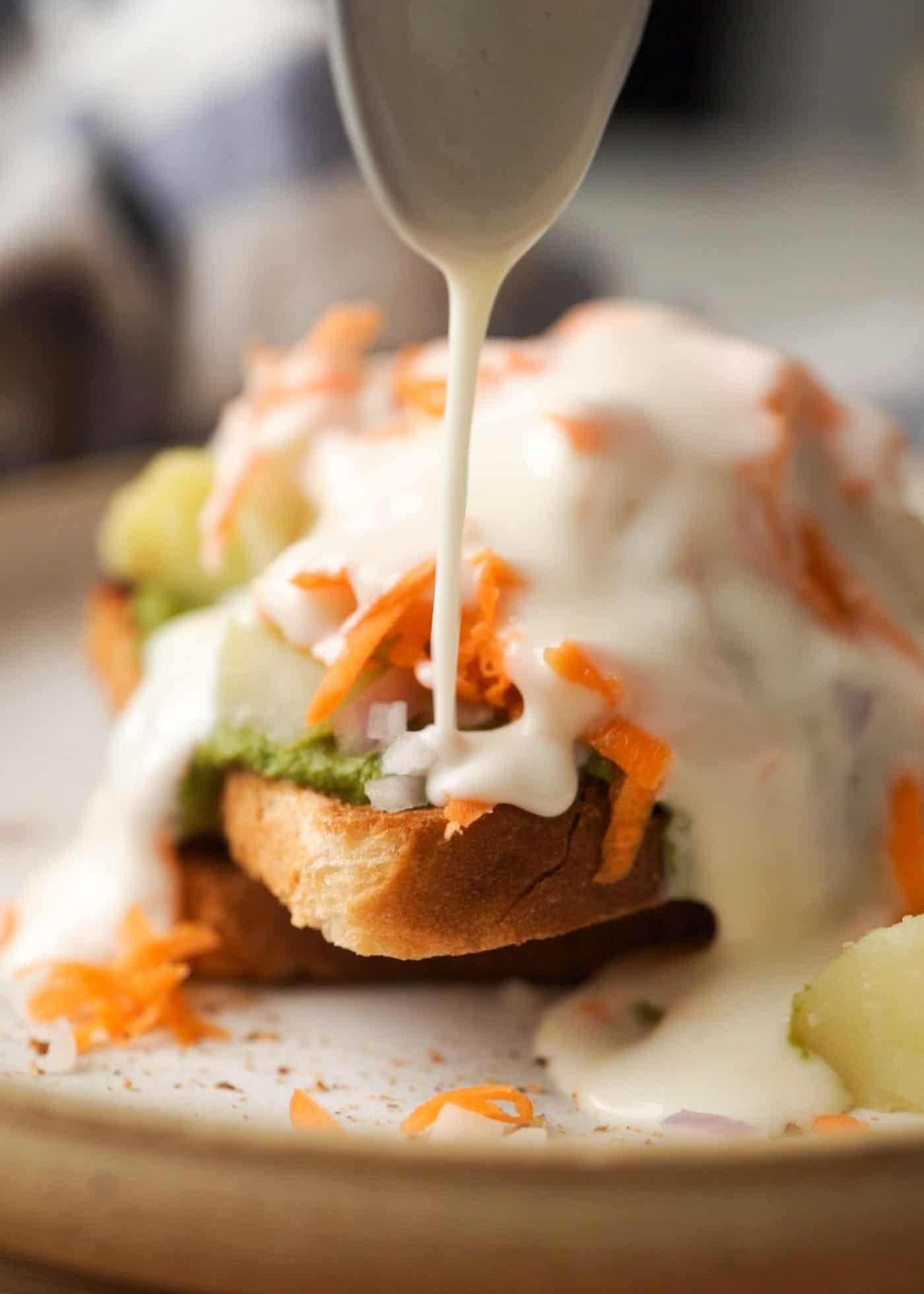 A picture of bread chaat being topped with curd