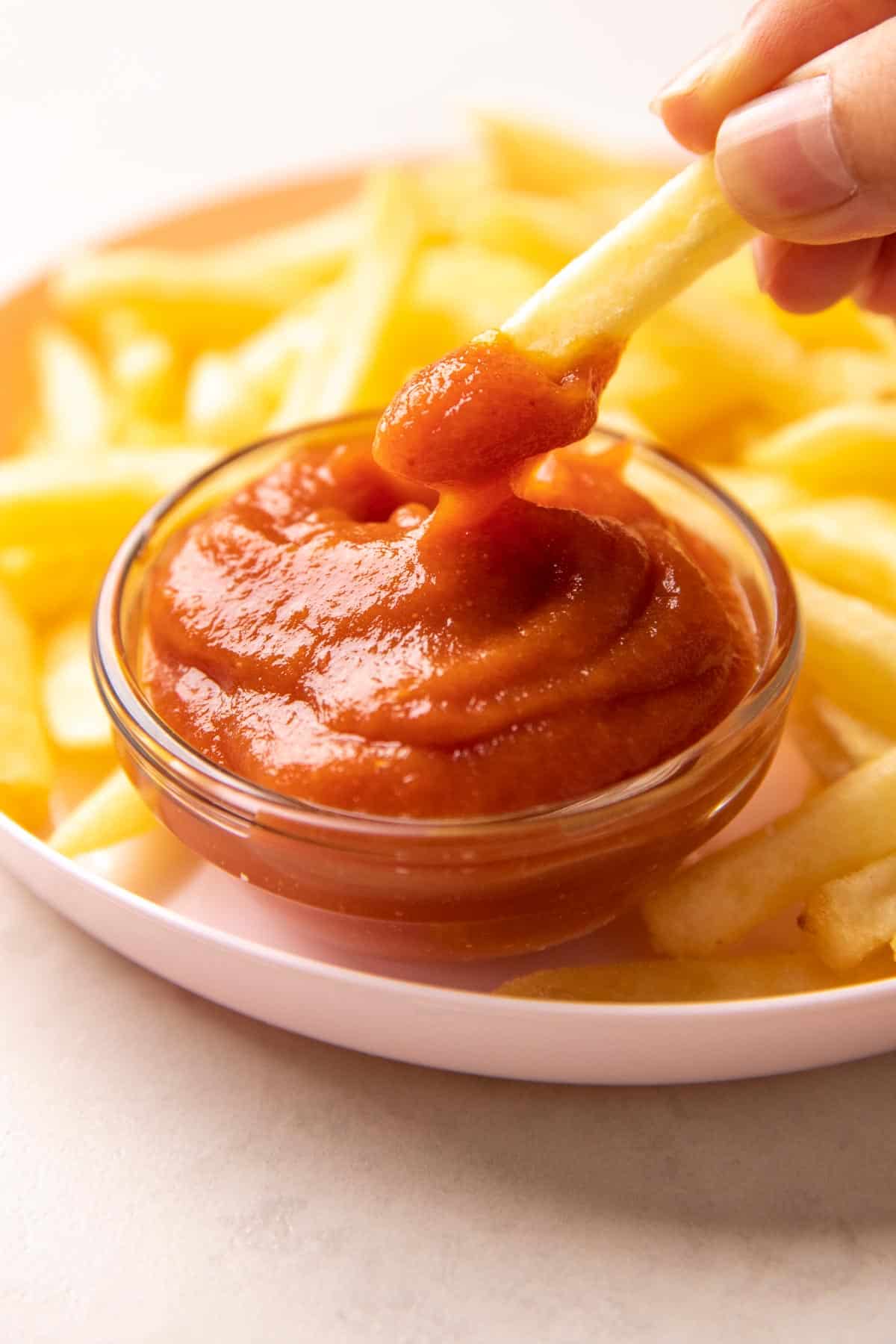 A french fry being dipped into a bowl of tomato ketchup