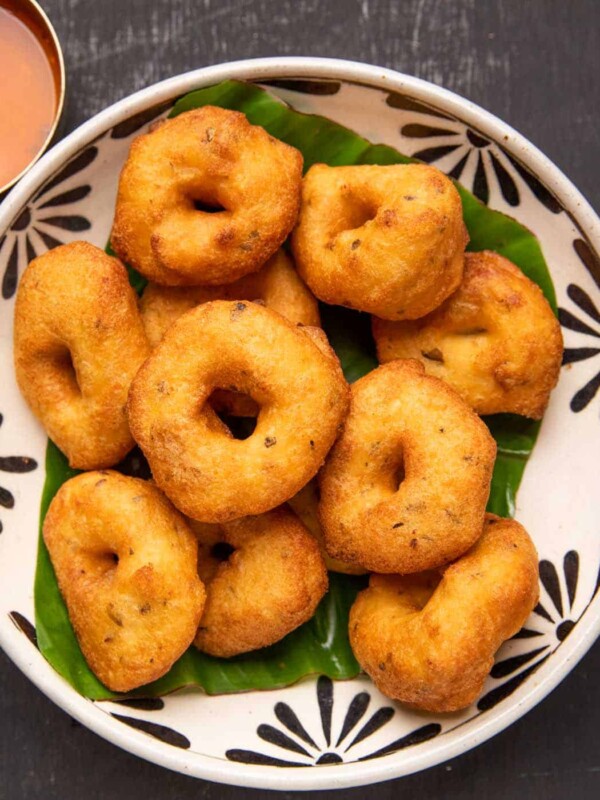 Medu vada served over a banana leaf in a bowl with chutney and sambar on the side