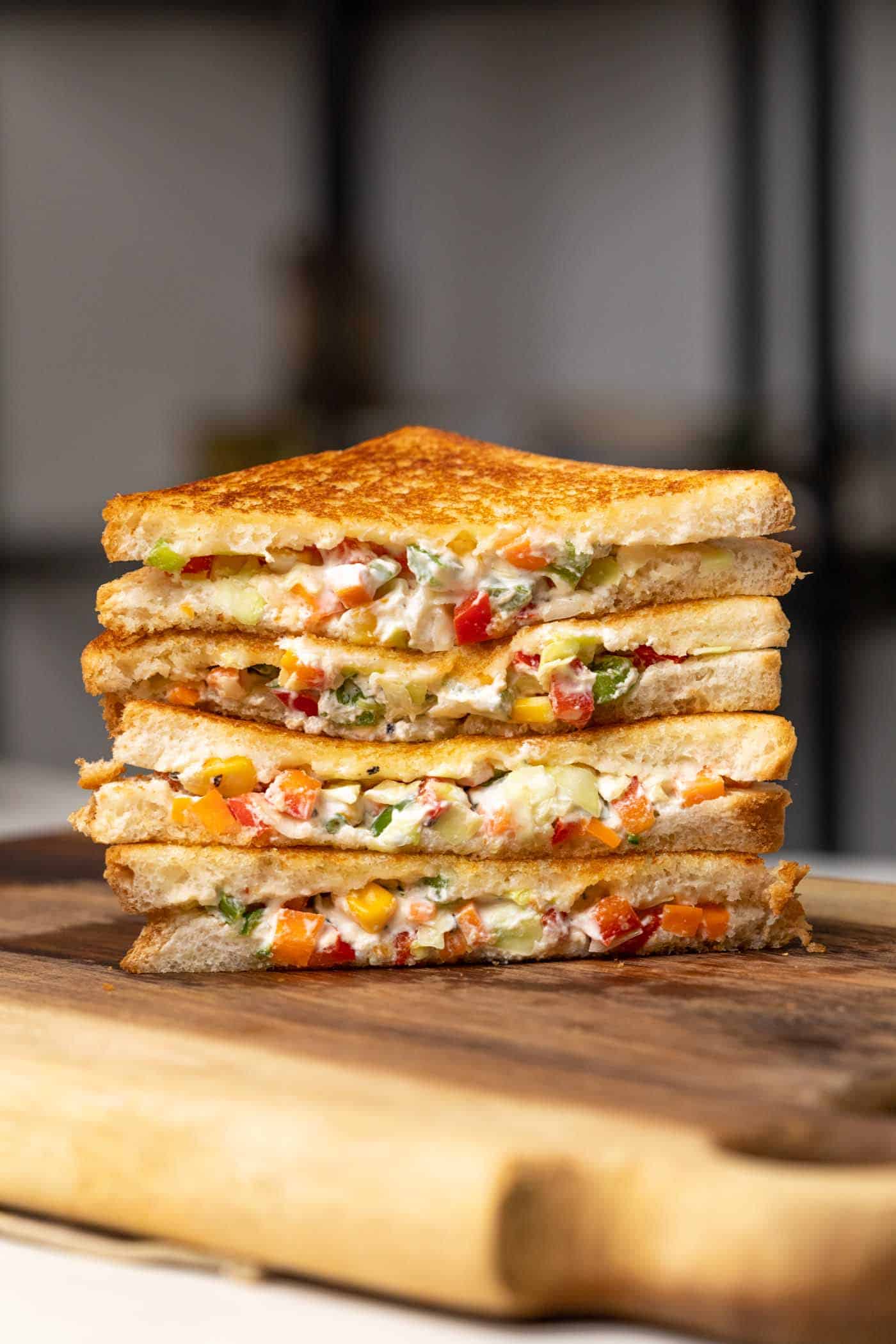 Image of sliced hung curd sandwich stacked one on top of the other on a wooden board