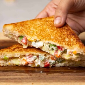A hand picking up a slice of hung curd sandwich