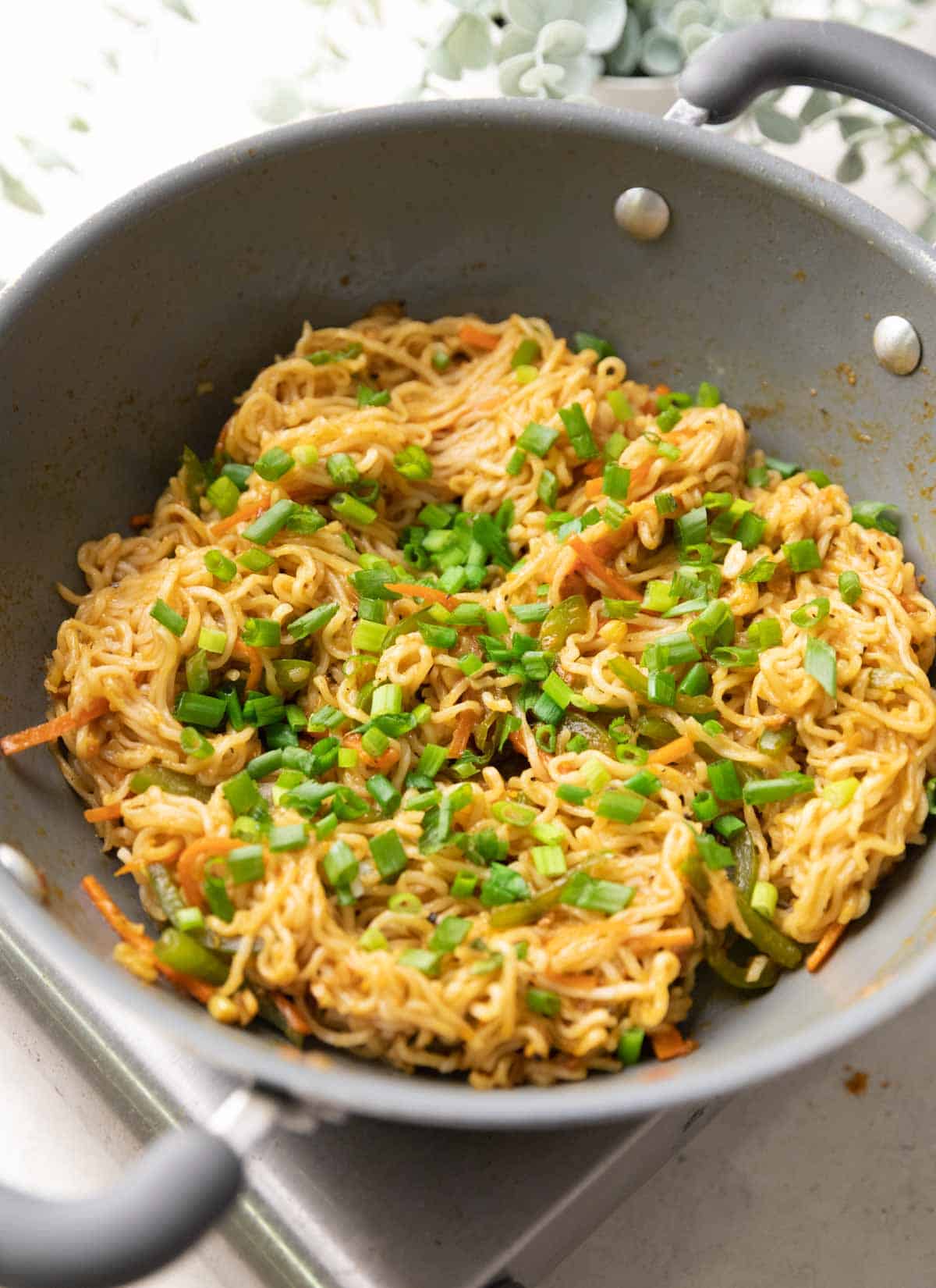 A shot of chinese maggi in a grey pan with spring onions