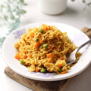 Masala maggi served in a white plate with a steel fork.
