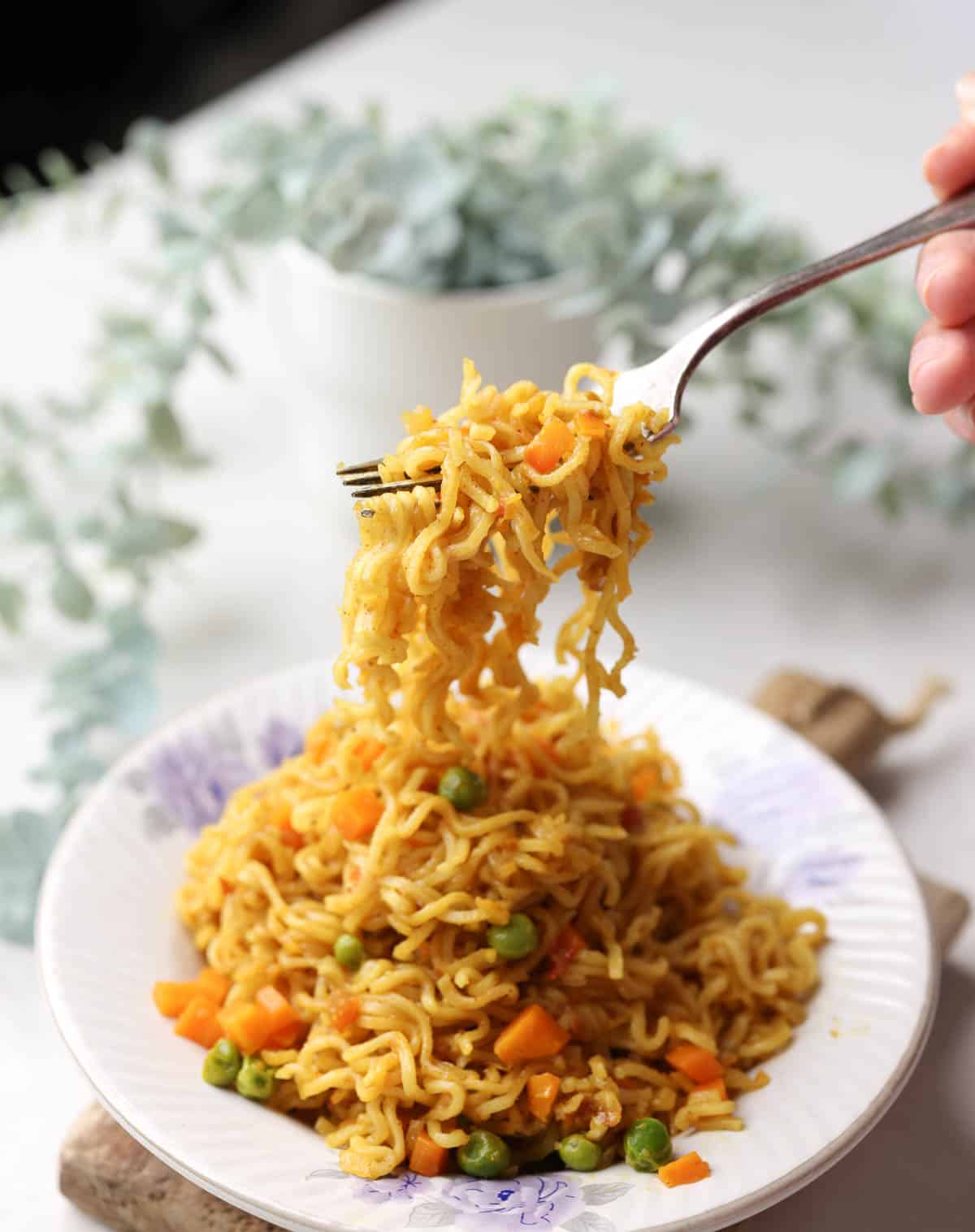 A shot of spicy masala maggi in a white plate with a fork full of noodles