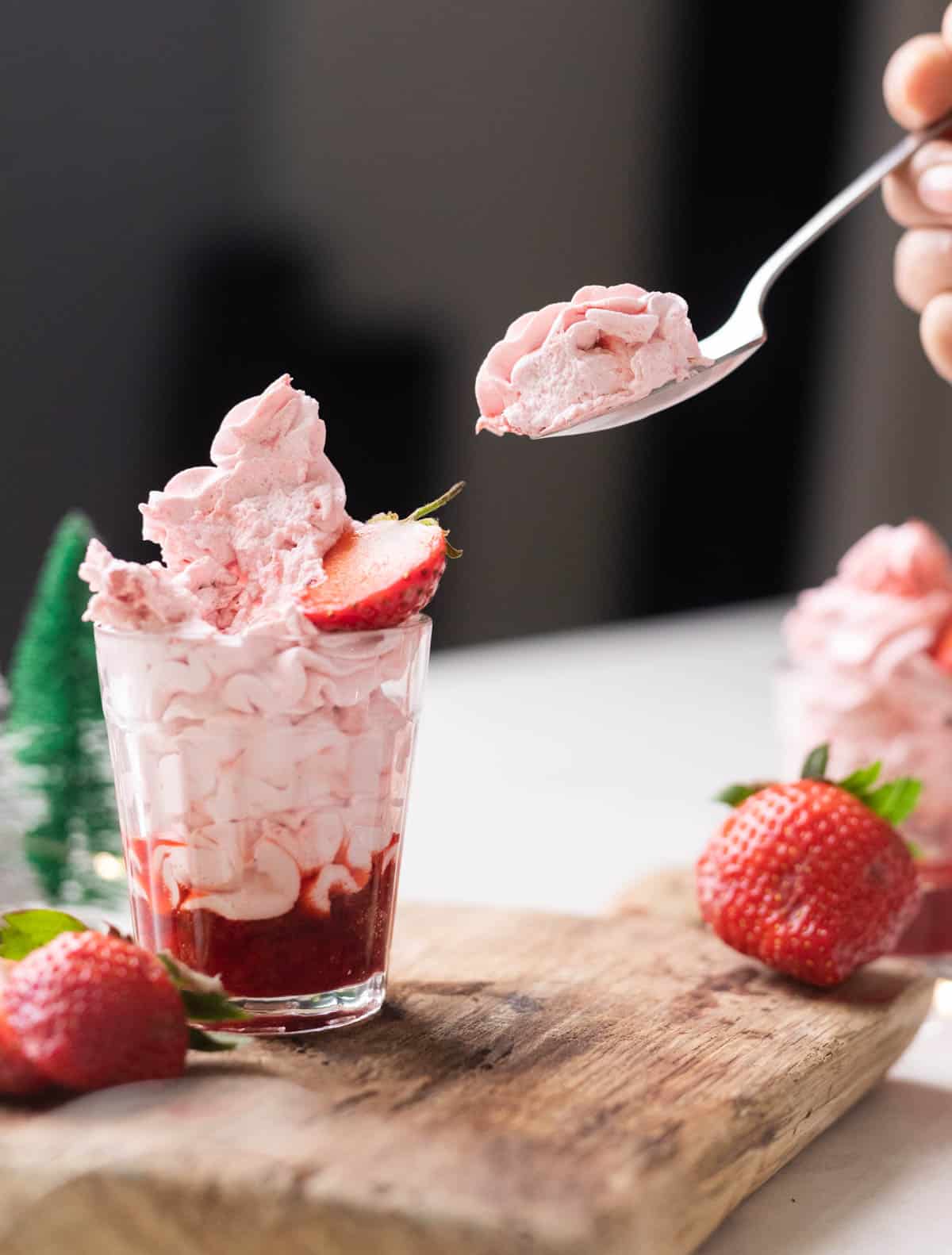 Strawberry mousse layered in a glass with strawberry compote topped with half a strawberry on a wooden board.