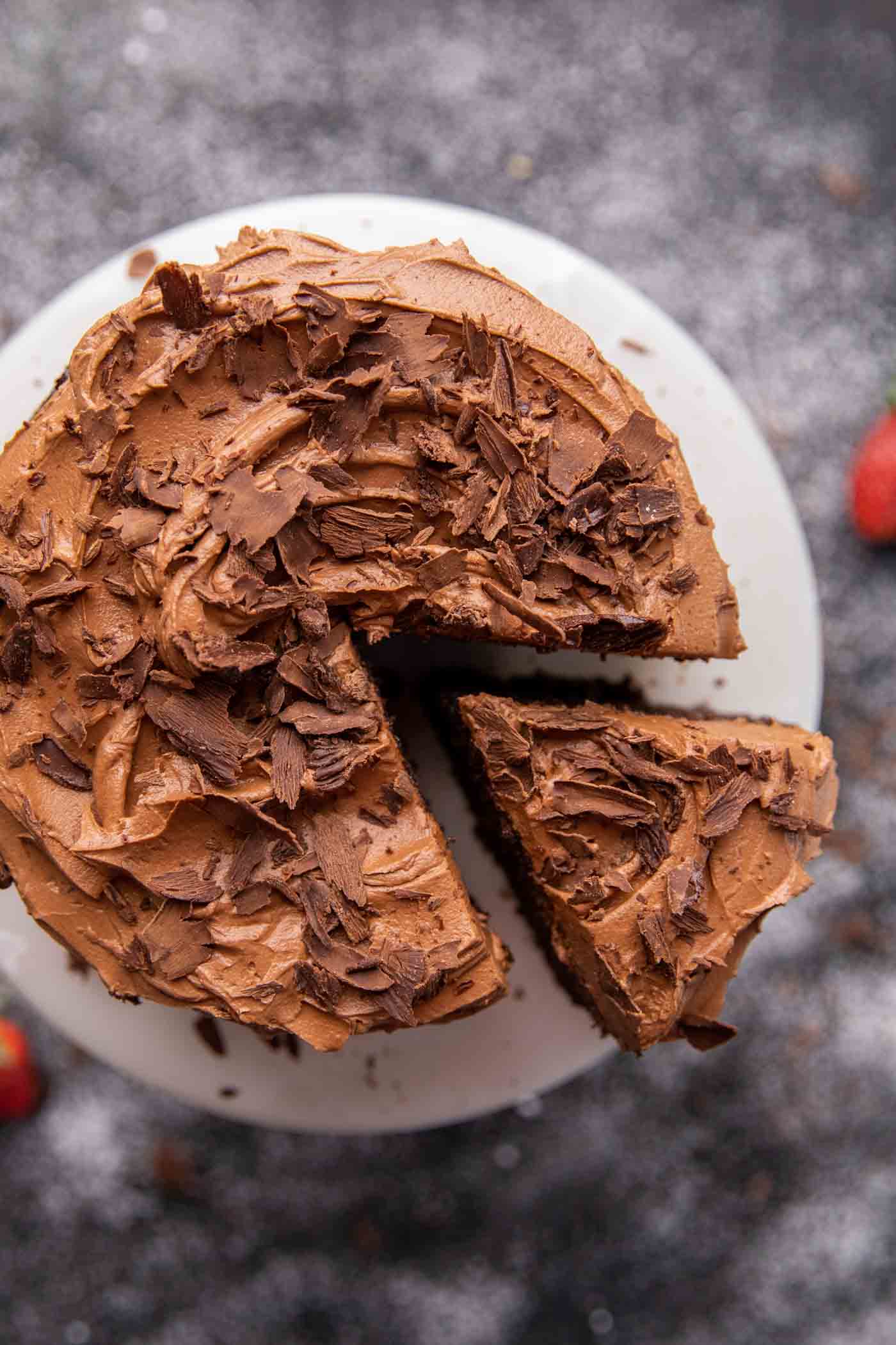 Chocolate cake on a white cake standtopped with chocolate buttercream frosting and chocolate flakes