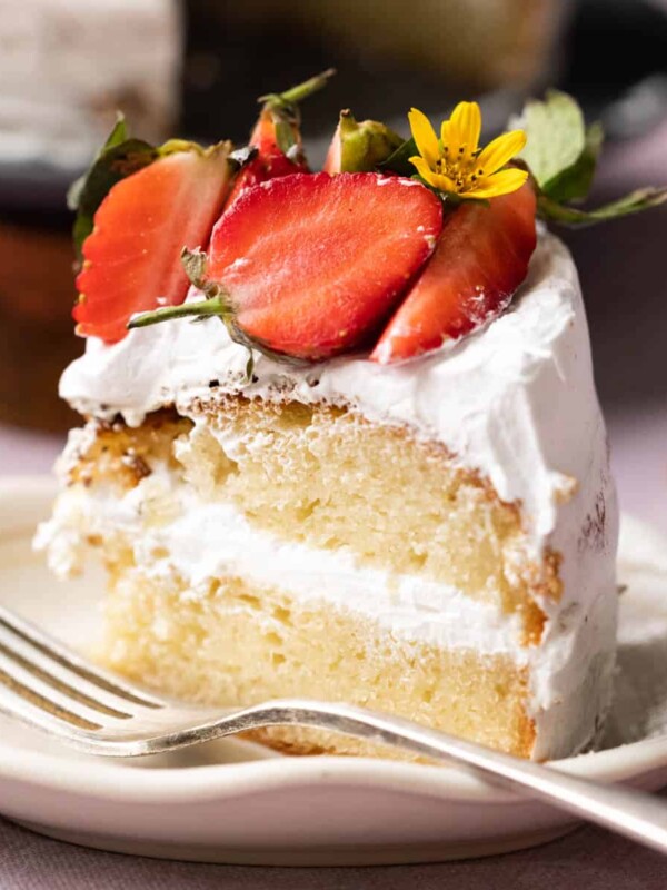 A slice of eggless vanilla cake layered with whipped cream and topped with strawberries
