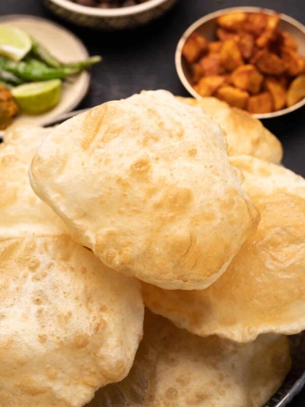 A plate of stacked bhature with a side of fried chilli, fried aloo and chole
