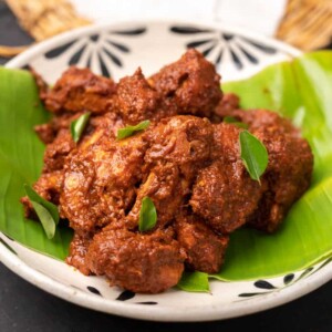 chicken ghee roast served on a white bowl over a plantain leaf