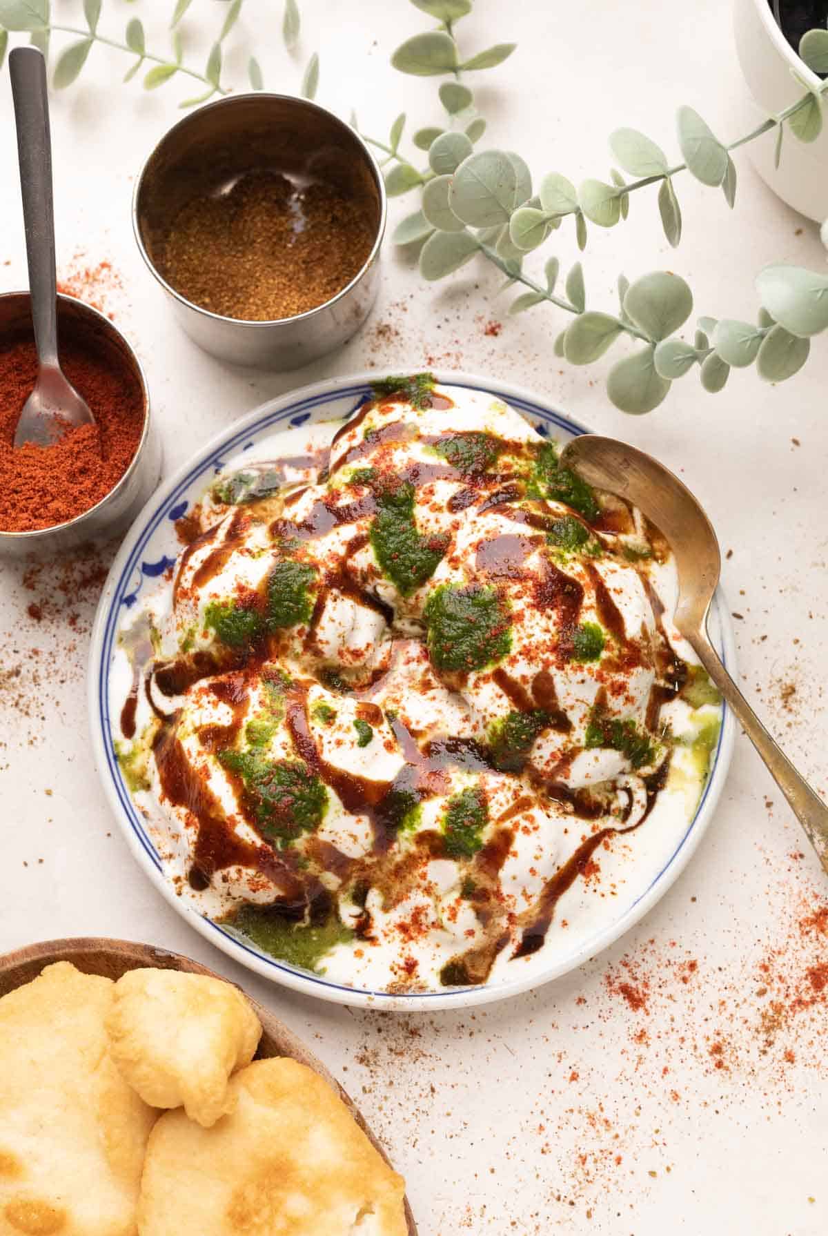 a plate of dahi vada with tamarind chutney, coriander mint chutney, extra vadas, coriander powder and red chilli powder