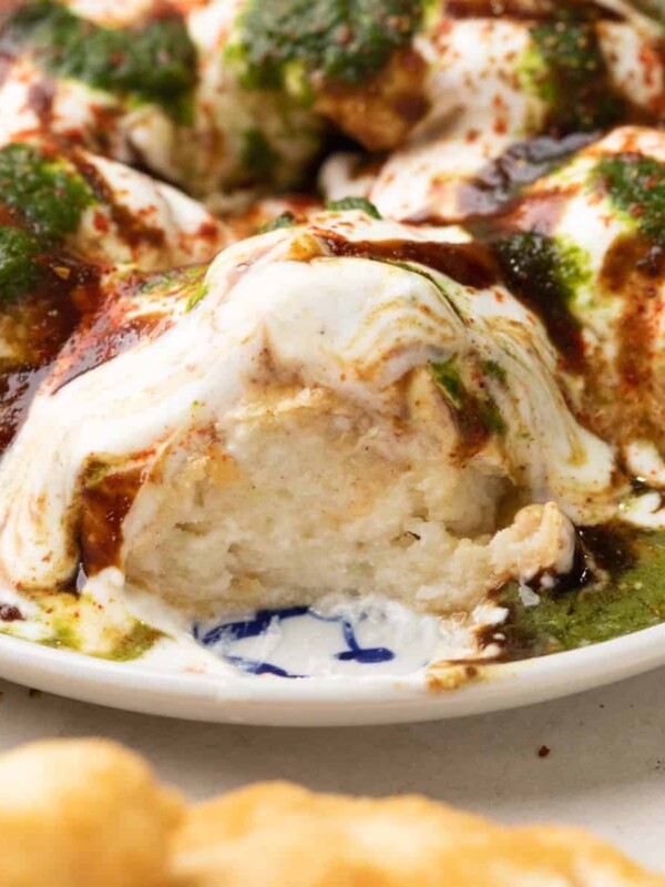 a plate of dahi vada with curd, tamarind chutney and coriander mint chutney drizzled on top.