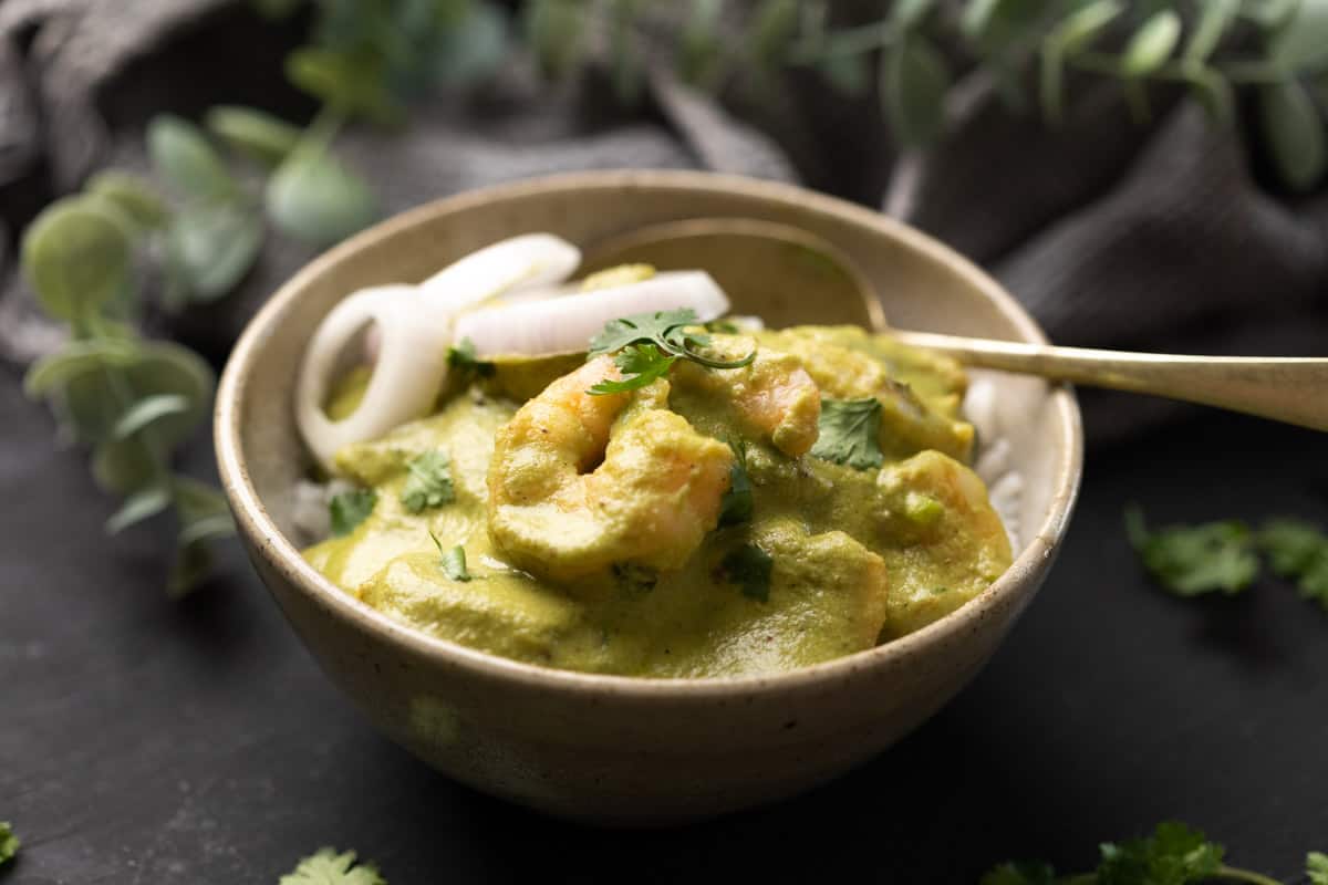 a bowl with white rice topped with green prawn curry with roundels of o