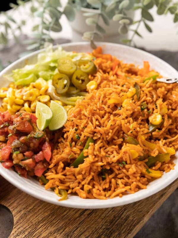 Instant Pot mexican rice served in a bowl with letttuce, corn, salsa, jalapenos and lime wedges on the side.