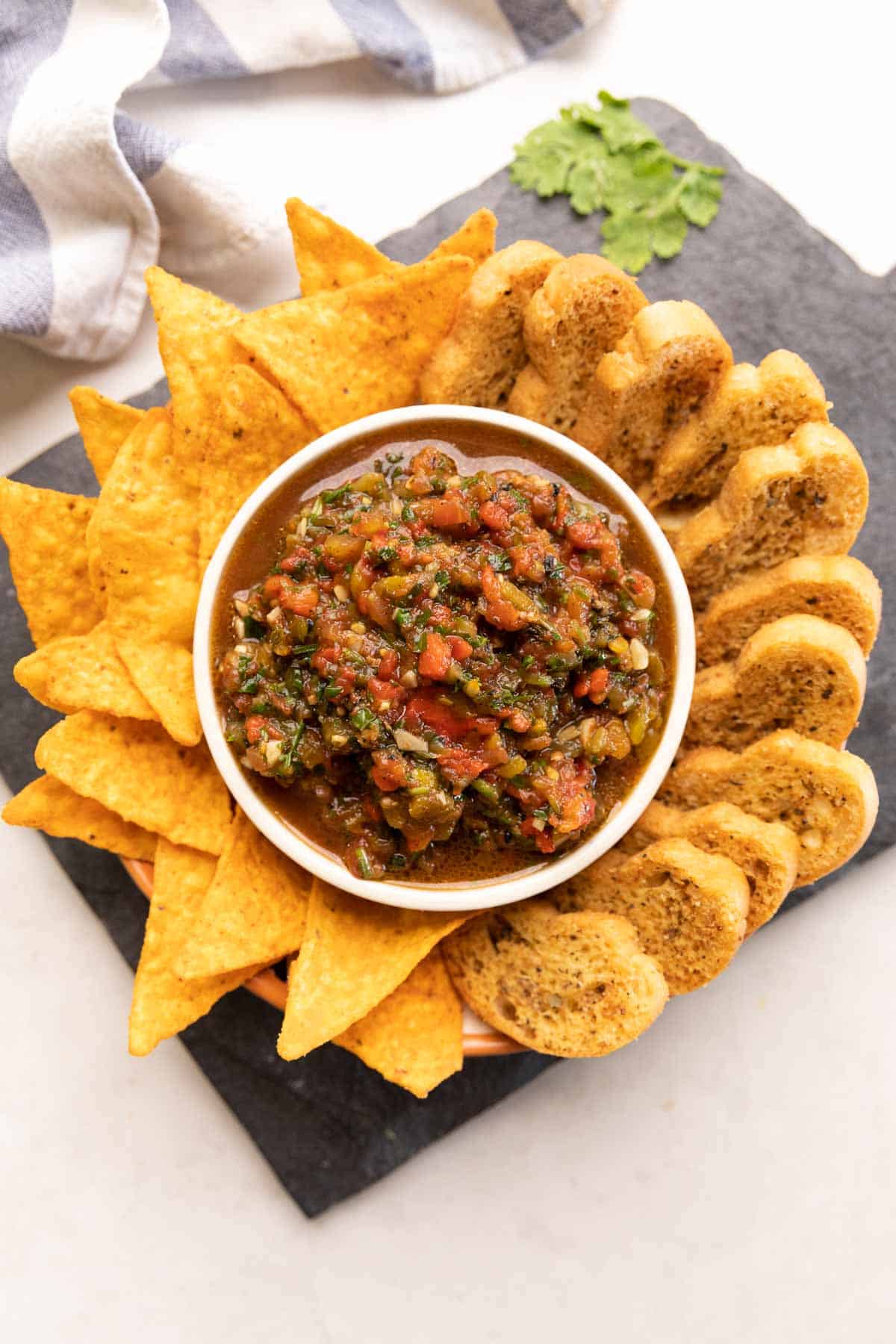 plate of nachos and crostini with a bowl of tomato salsa in the middle