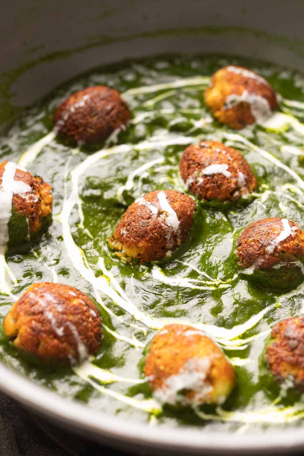The Healthy Palak Paneer Kofta Curry in a pan with cream drizzled on top