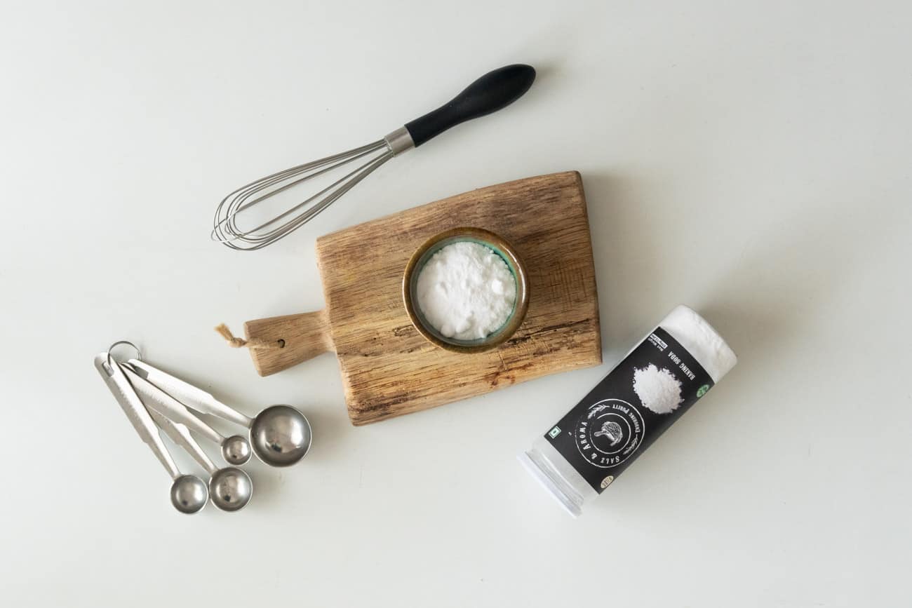 picture of baking soda in a cup on a chopping board with a whisk and measuring spoons on the side