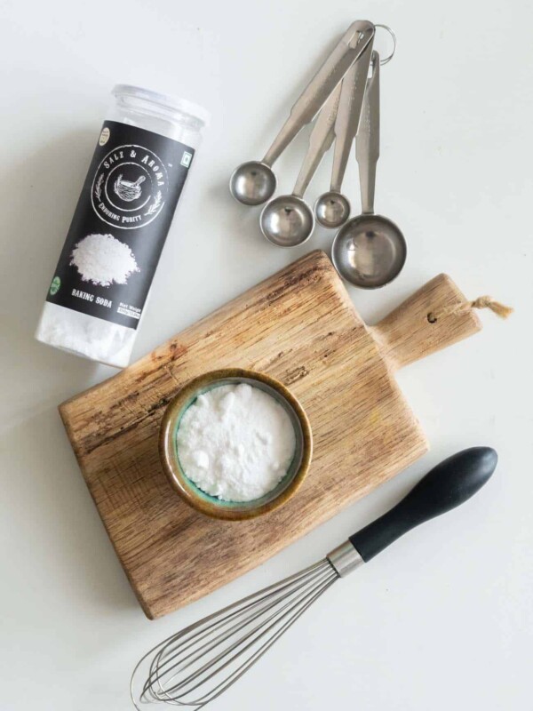 picture of baking soda in a cup on a chopping board with a whisk and measuring spoons on the side
