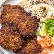 top shot of chapli kebabs served in a white plate with naan, onion, lemon, and coriamder
