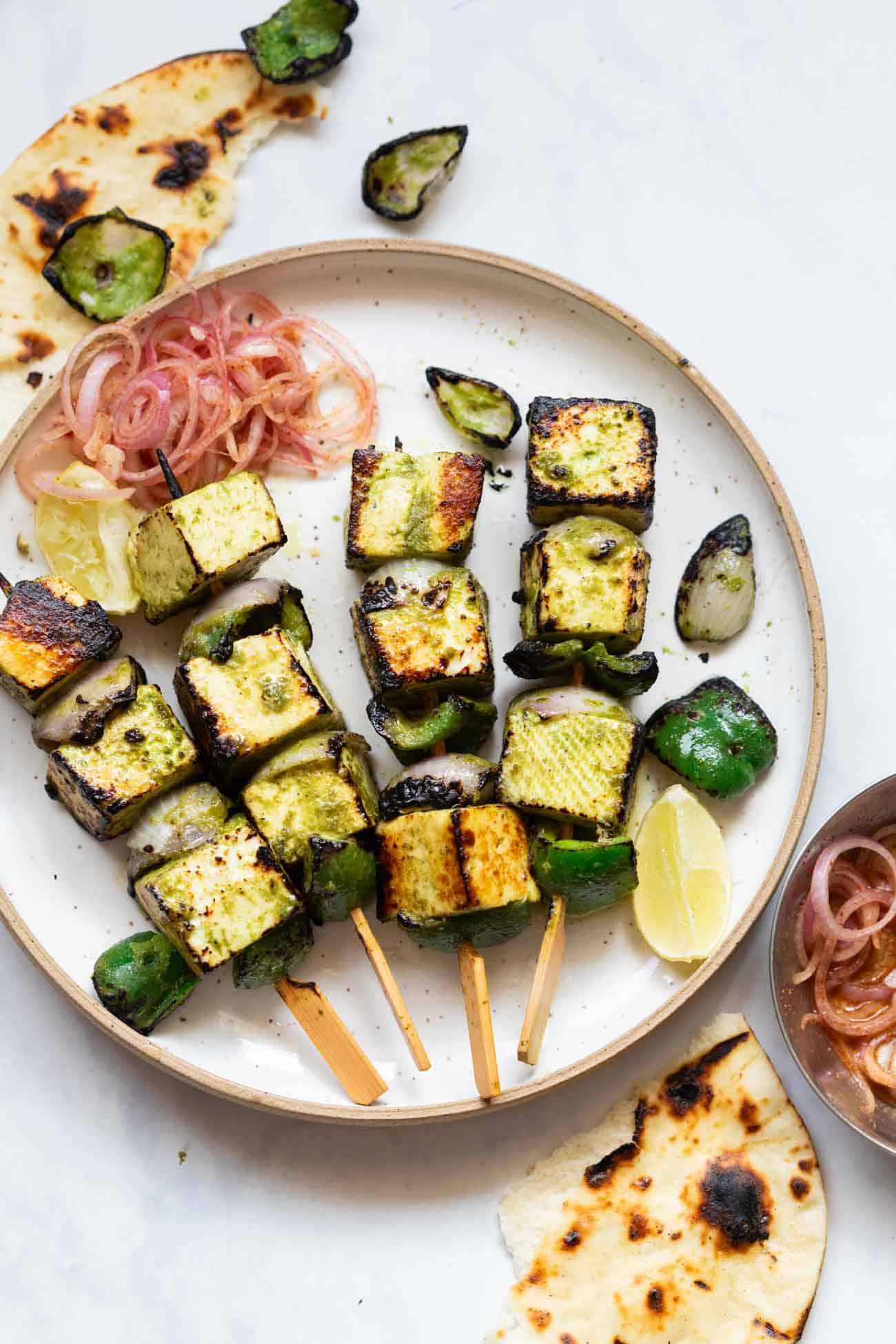 a shot of hariyali paneer tikka on skewers placed on a white plate