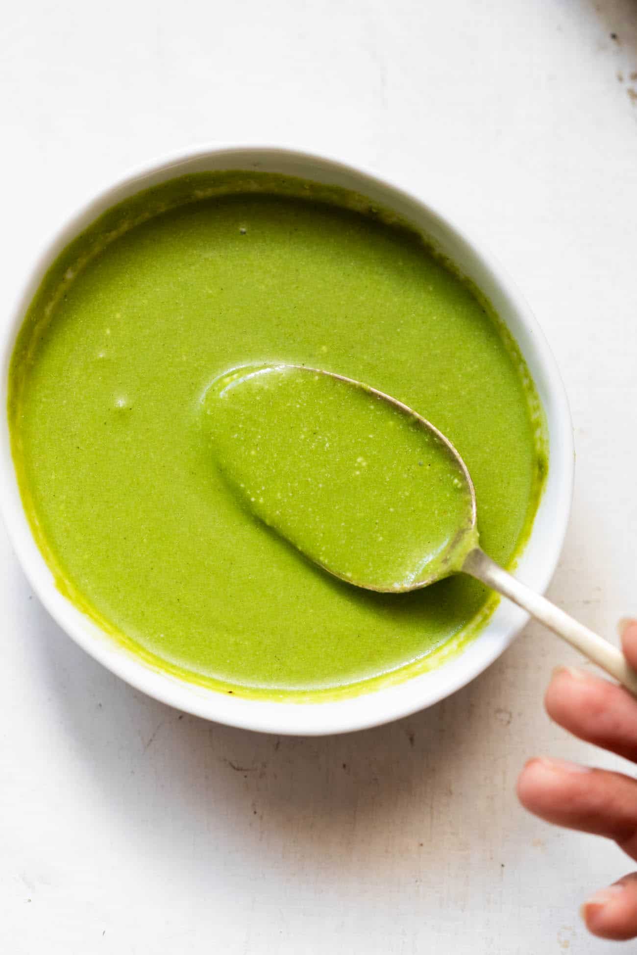 mint chutney served in a white bowl with a spoonful of chutney being taken out