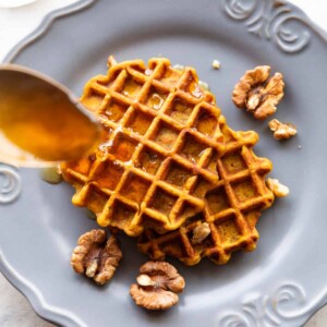 Spoon drizzling honey over two pumpkin waffles served on a plate