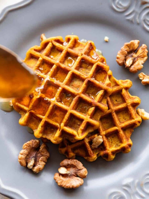 Spoon drizzling honey over two pumpkin waffles served on a plate