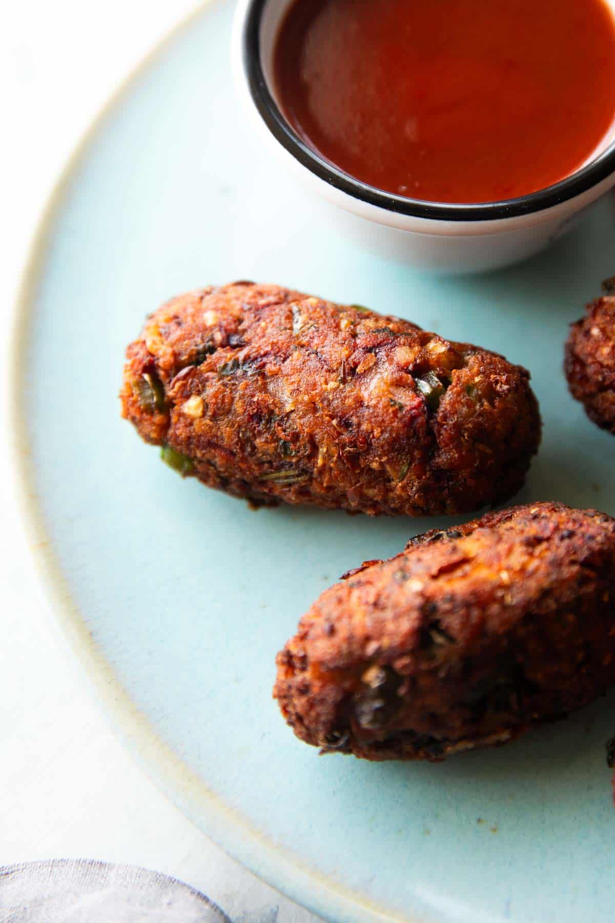 a close up shot of sprouts cutlet on a blue plate with ketchup on the side