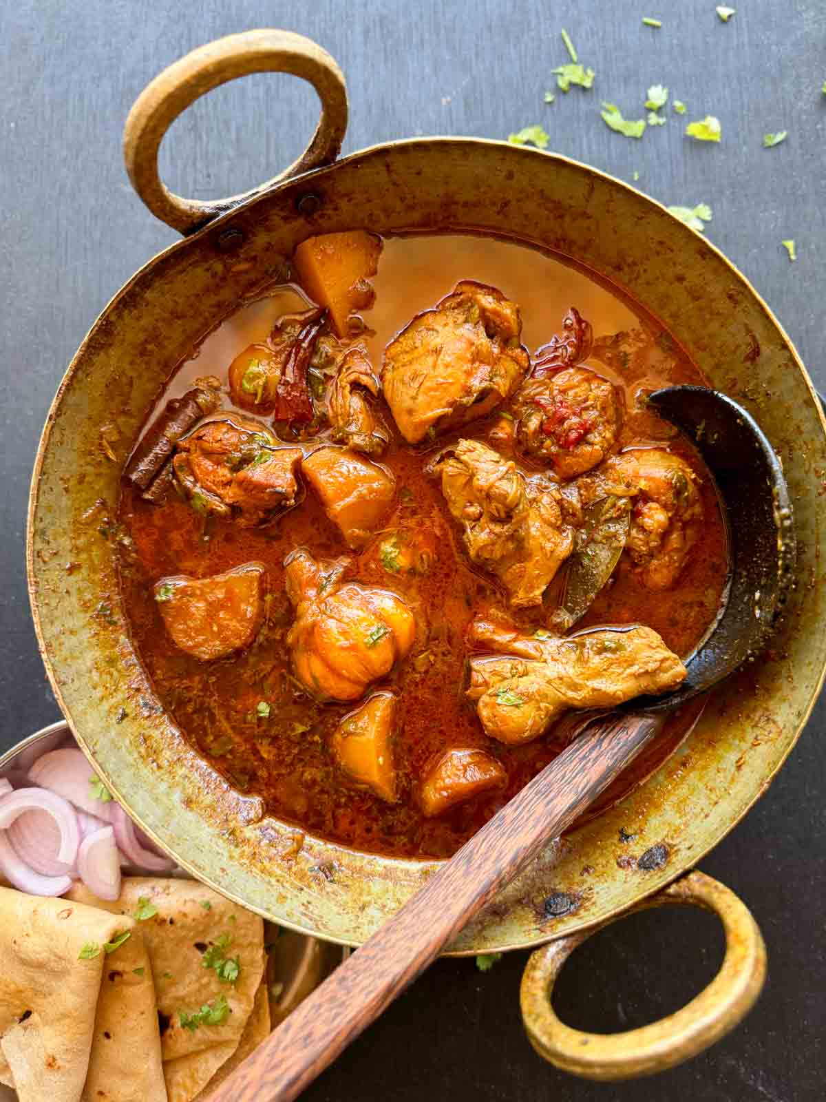 Bihari chicken curry served in a kadhai with roti and onions on the side