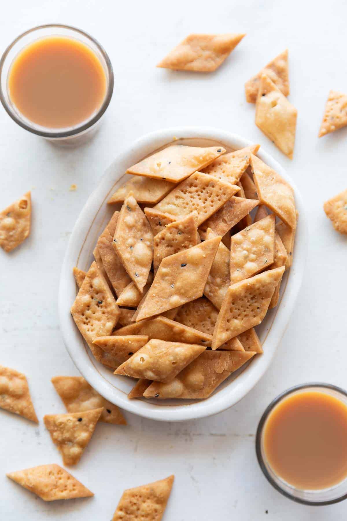 Picture of namak para in a white bowl with cups of chai around it