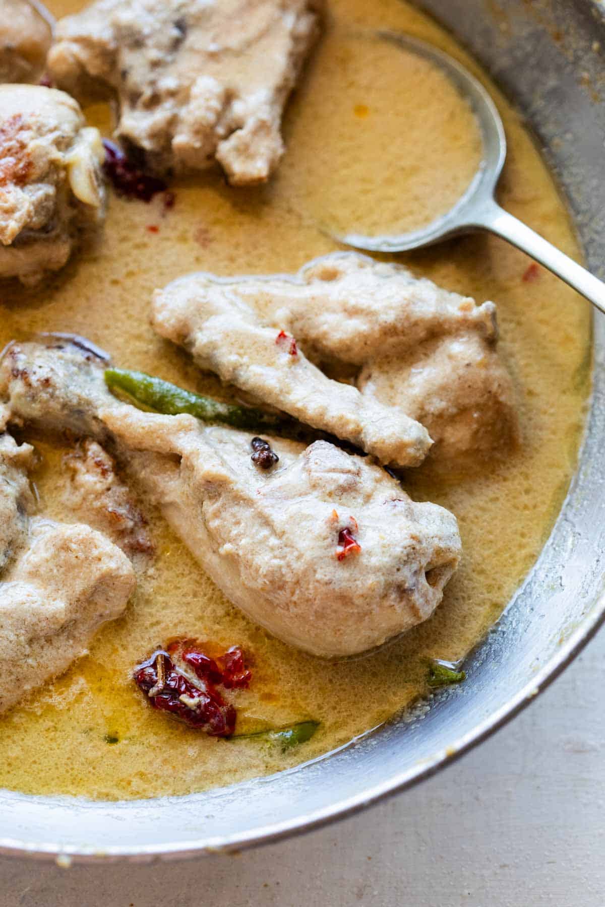Cooked chicken rezala in an aluminium kadhai with a spoon