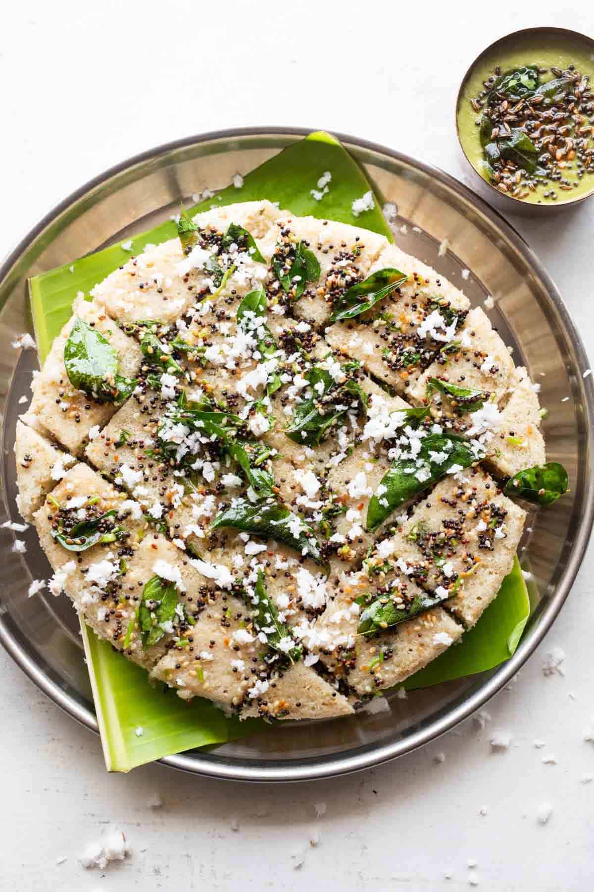 Jowar dhokla served on a banana leaf on a plate with coconut chutney on the side