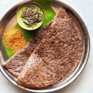 Ragi dosa served in a steel plate on a banana leaf with coconut chutney and podi