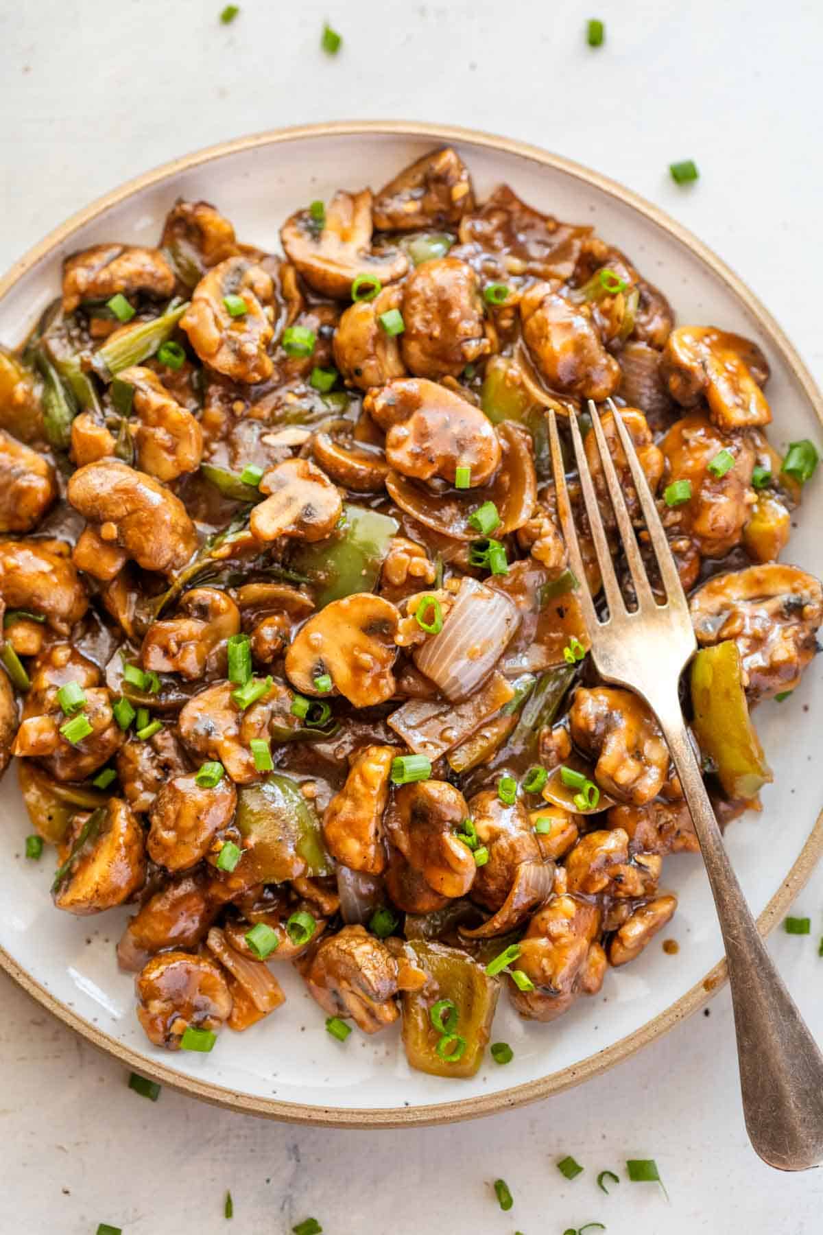 Mushroom chilli on a white plate with a fork on the side