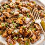Mushroom chilli on a white plate with a fork on the side