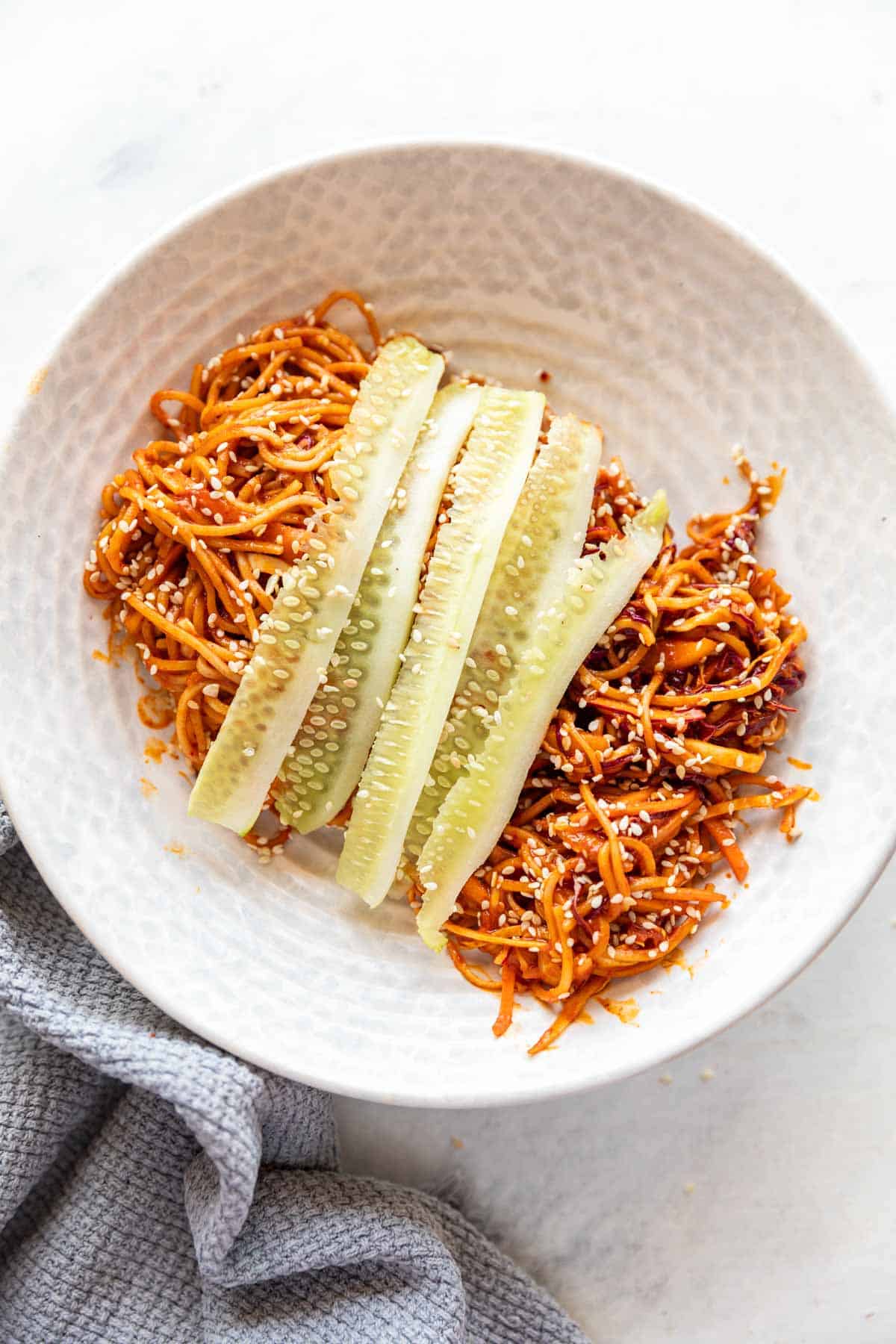 Bibim Guksu garnished with thin slices of cucumber cut in a white bowl