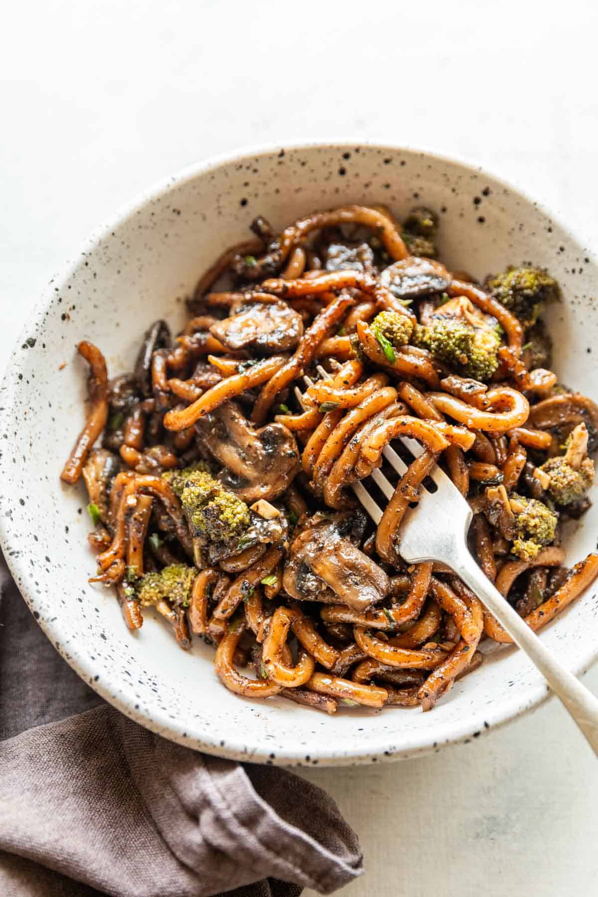 Black pepper udon noodles served in a white bowl with fork