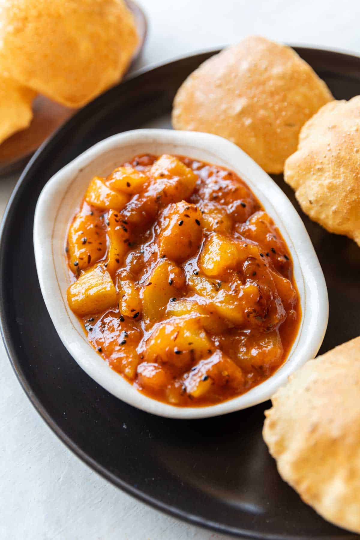 raw mango chutney in a white bowl served with hot pooris