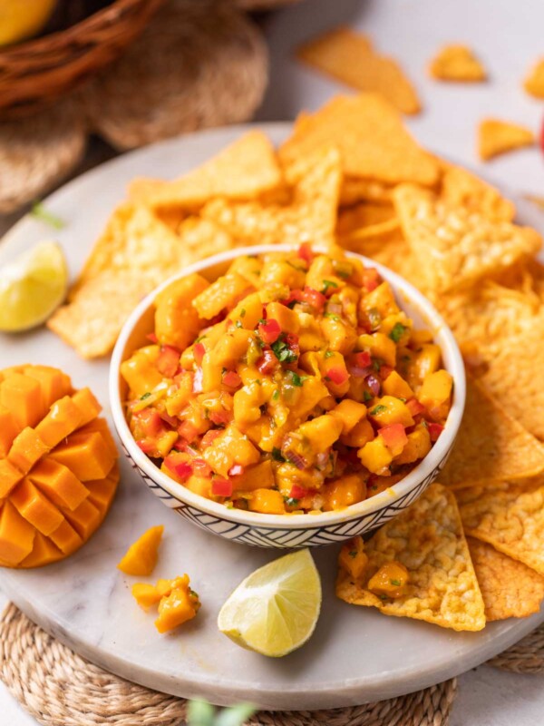 fresh and juicy mango salsa served with nacho chips and other accompaniments in a white bowl