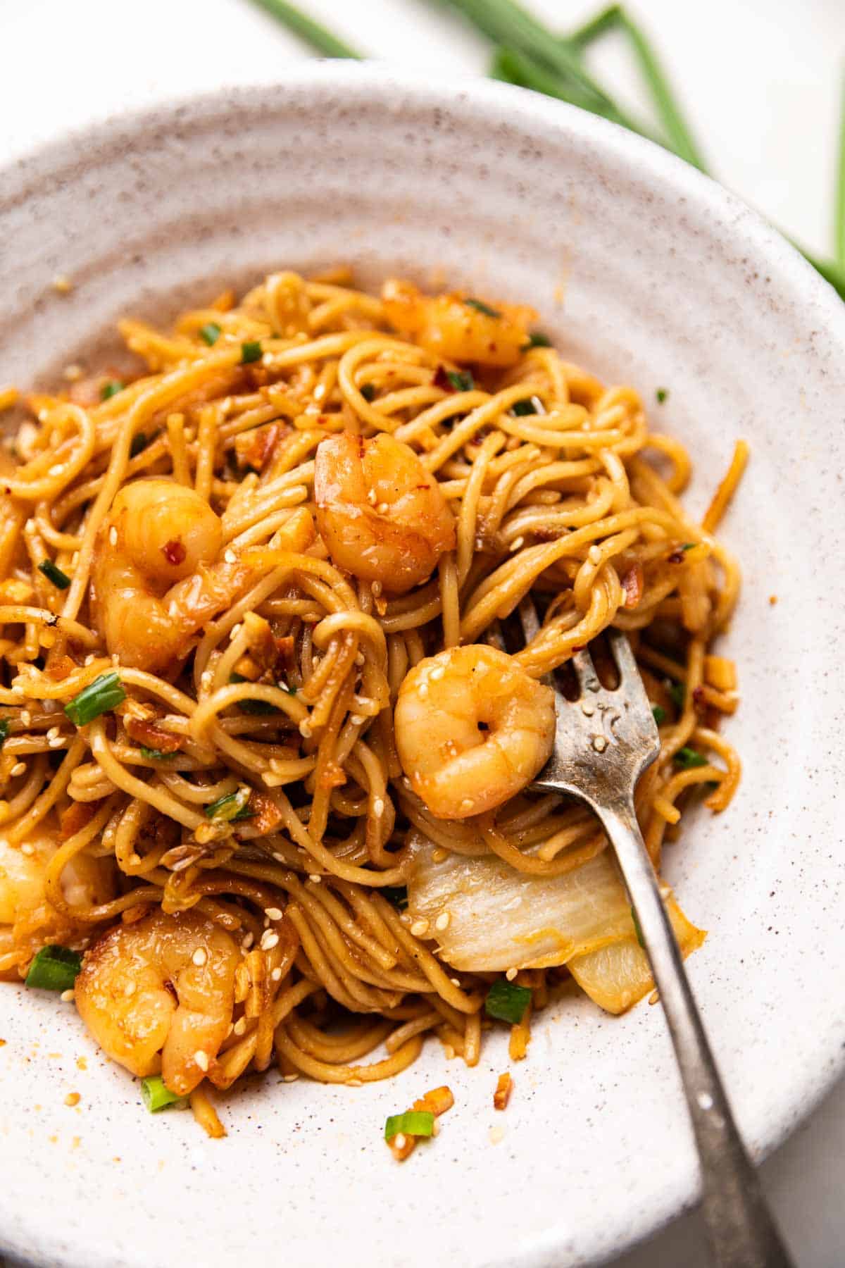 chilli garlic prawn noodles served in a white bowl with a fork