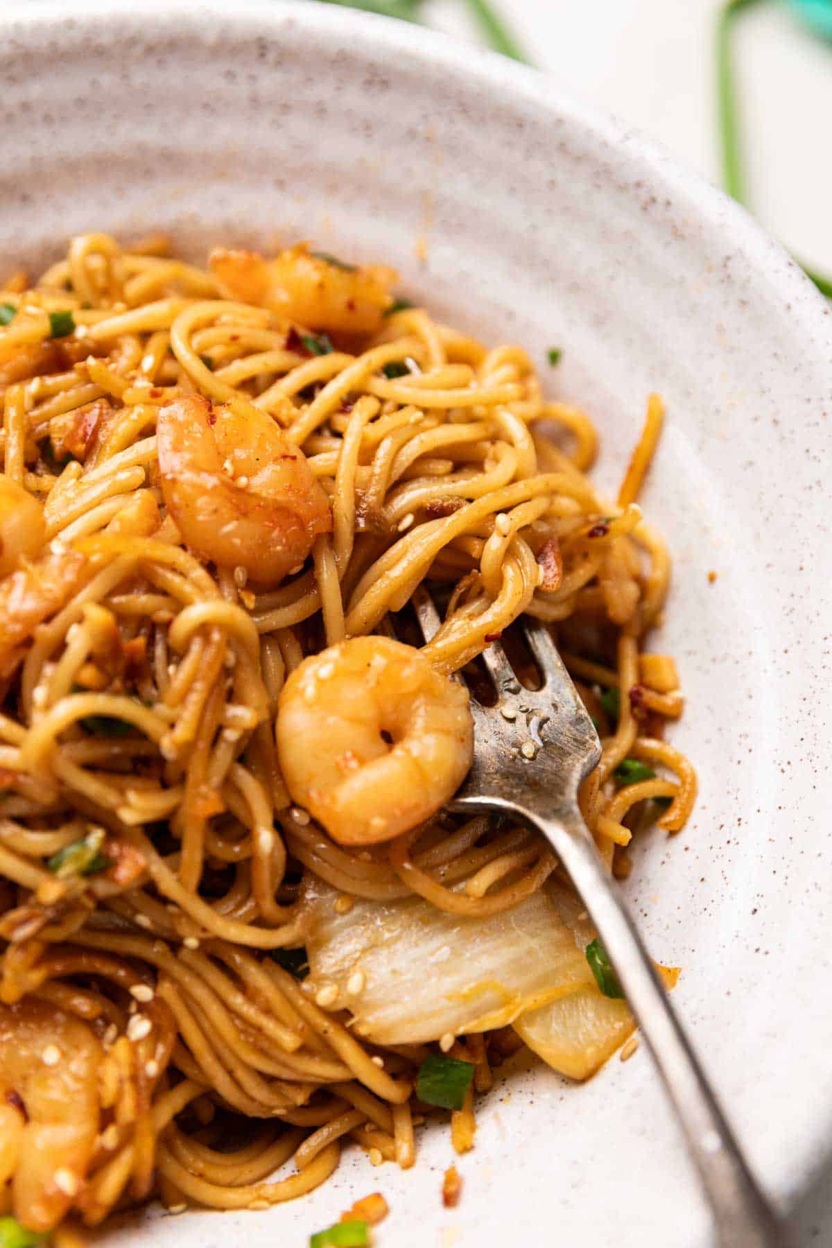 close up of chilli garlic prawn noodles served in a white bowl with a fork
