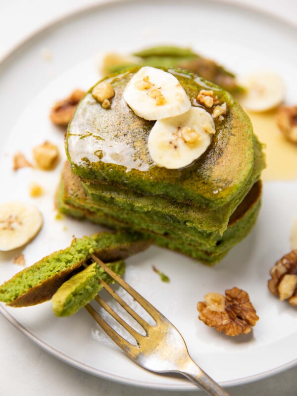 stacked spinach banana pancakes topped with banana slices, walnuts and honey and served with a fork