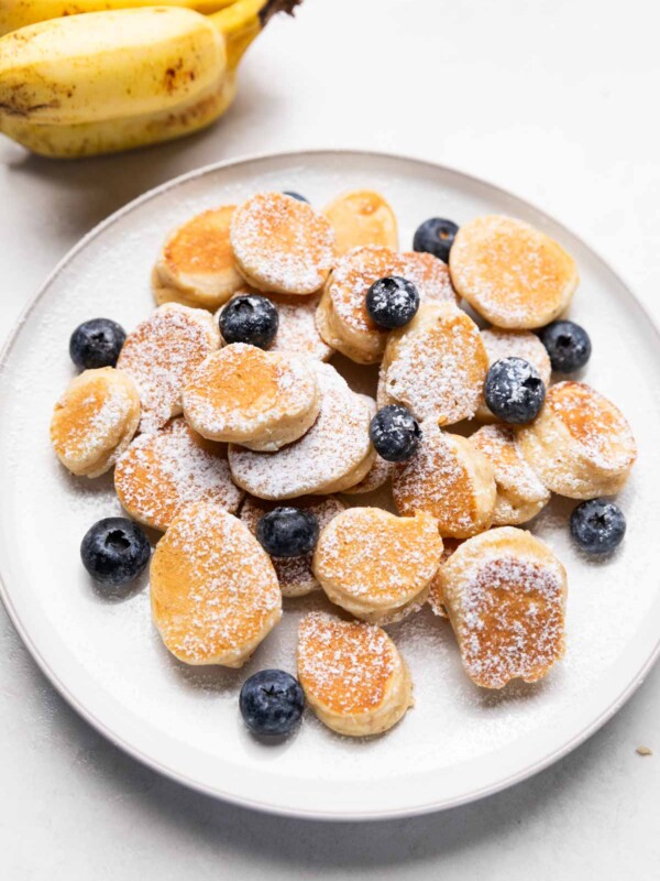 mini banana pancake bites garnished with powdered sugar & blueberries served on a white plate