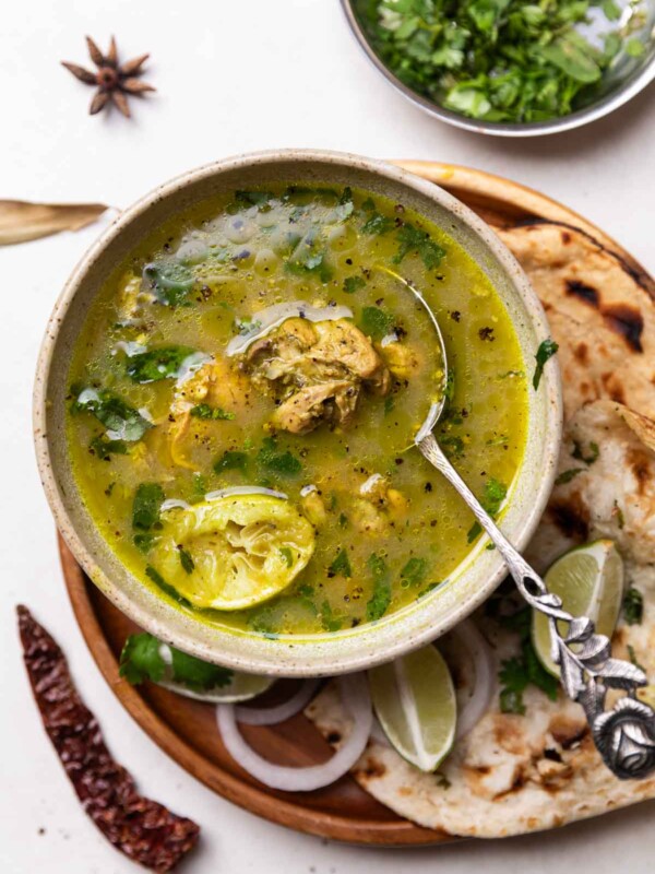 chicken shorba served in a bowl with spoon along with naan, chopped onion and lemon wedges