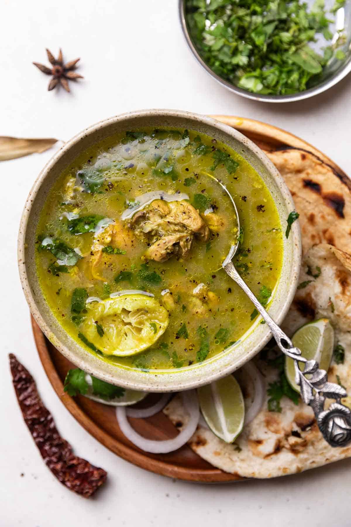 chicken shorba served in a bowl with spoon along with naan, chopped onion and lemon wedges
