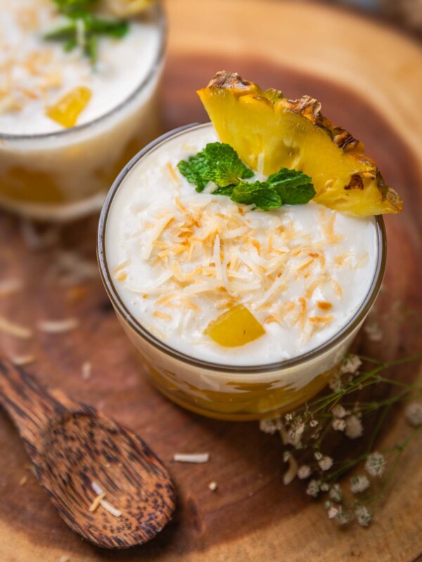 coconut pudding with pineapple jelly garnished with toasted coconut flakes, pineapple slice and mint leaves and served in shot glasses