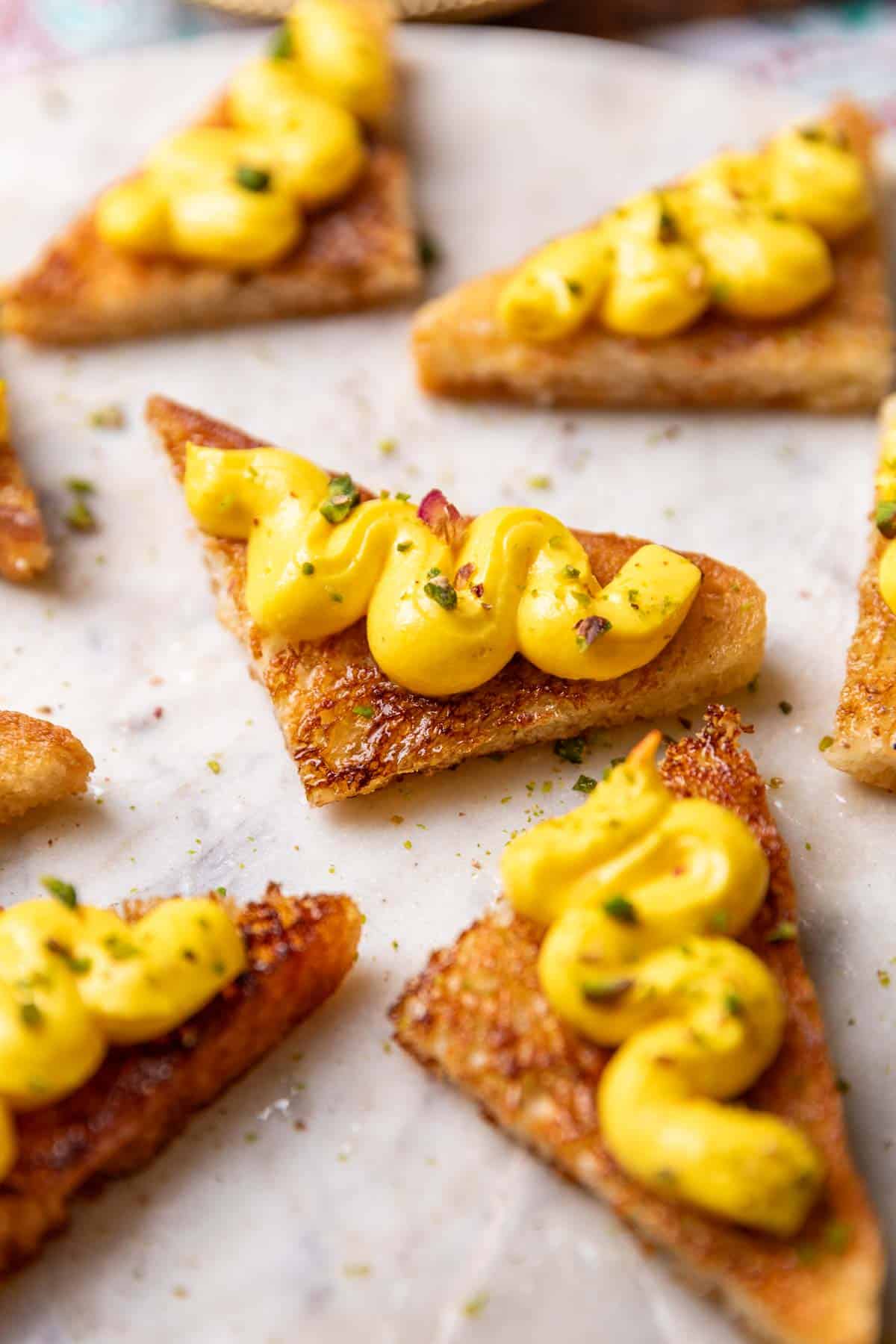 close up of rasmalai toasts garnished with pistachios and served on a white platter